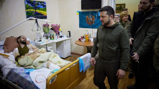 Presiden Ukraina Volodymyr Zelensky (kedua kanan) berbicara dengan seorang prajurit yang terluka dan mendapatkan perawatan di salah satu rumah sakit militer di Kyiv, Ukraina, Minggu (13/3/2022). [Kantor Kepresidenan Ukraina / AFP]