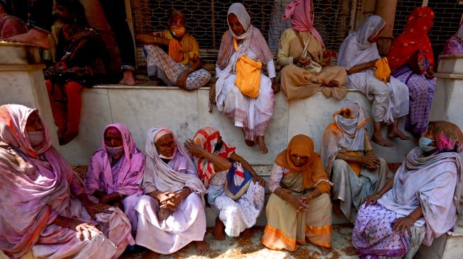 Para janda yang berlumuran Gulal (bubuk warna) duduk di dalam kuil saat mereka berpartisipasi dalam perayaan Holi di sebuah kuil di Vrindavan, India, Selasa (15/3/2022). [Money SHARMA / AFP]