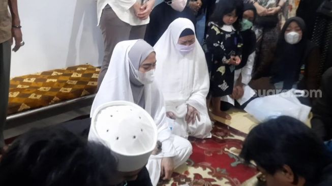 April Jasmine (kiri) menangisi jenazah sang ayah Omar Mardjuki yang meninggal dunia Selasa (15/3/2022) mala. [Evi Ariska/Suara.com]