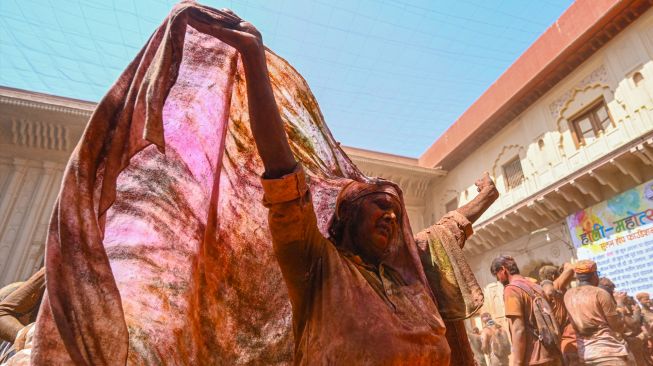 Seorang janda yang berlumuran Gulal (bubuk warna) menari saat mereka berpartisipasi dalam perayaan Holi di sebuah kuil di Vrindavan, India, Selasa (15/3/2022). [Money SHARMA / AFP]