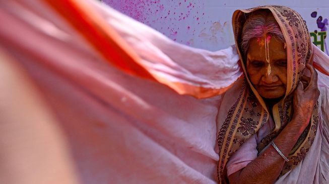 Seorang janda yang berlumuran Gulal (bubuk warna) berpartisipasi dalam perayaan Holi di sebuah kuil di Vrindavan, India, Selasa (15/3/2022). [Money SHARMA / AFP]