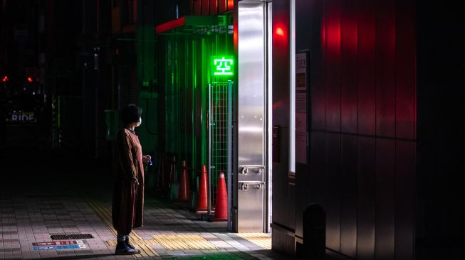 Seorang wanita berdiri di depan pintu masuk stasiun kereta bawah saat pemadaman listrik yang berlangsung setelah gempa berkekuatan 7,3 SR mengguncang wilayah Jepang Timur di Tokyo, Jepang, Kamis (17/3/2022). [Philip FONG / AFP]
