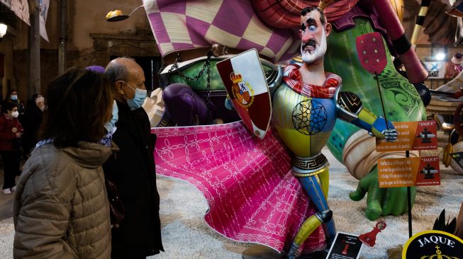 Para pengunjung berjalan melewati boneka fallas yang dipamerkan saat festival Las Fallas di Valencia, Spanyol, Rabu (16/3/2022). [Jose Jordan / AFP]