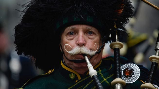 Seorang pria berkumis meniup alat musik bagpipe miliknya saat parade perayaan Hari St. Patrick di New York, Amerika Serikat, Kamis (17/3/2022). [Ed JONES / AFP]