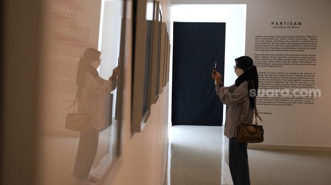 Pengunjung mengambil gambar  karya seni dalam pameran tunggal karya Otty Widasary yang bertajuk "Partisan" di Gedung D, Galeri Nasional, Jakarta, Minggu (20/3/2022). [Suara.com/Angga Budhiyanto]