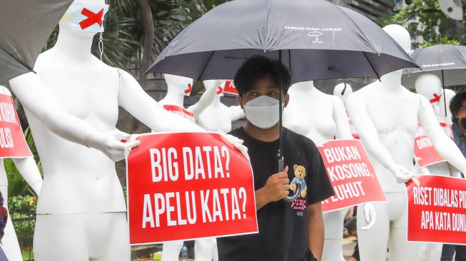 Sejumlah aktivis mengenakan masker bertanda silang berdiri disamping manekin saat melakukan aksi di depan Polda Metro Jaya, Jakarta Selatan, Senin (21/3/2022). [Suara.com/Alfian Winanro]