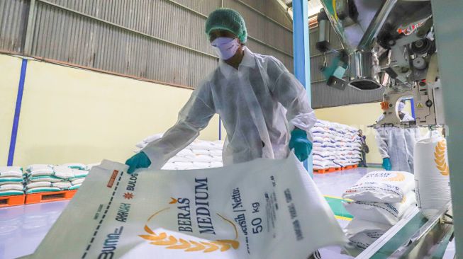 Pekerja mengoperasikan mesin Rice To Rice (RTR) untuk mengisi karung beras medium di Gudang RTT Bulog, Kelapa Gading, Jakarta Utara, Rabu (23/3/2022). [Suara.com/Alfian Winanto]