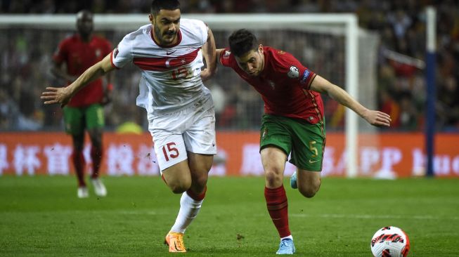 Bek Turki Ozan Kabak (kiri) bersaing dengan bek Portugal Raphael Guerreiro saat pertandingan sepak bola play-off kualifikasi Piala Dunia 2022 antara Portugal dan Turki di stadion Dragao, Porto, Portugal, Kamis (24/3/2022). [MIGUEL RIOPA / AFP]