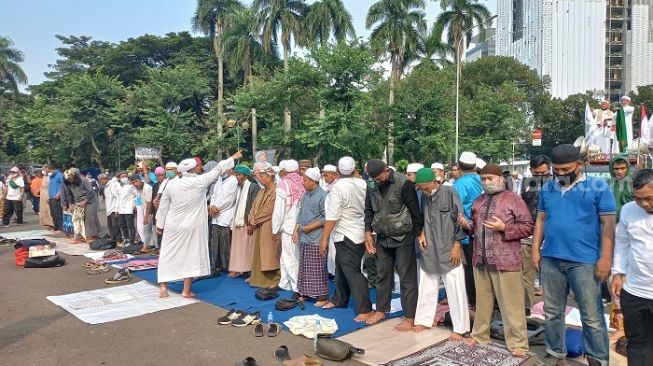 Massa pendemo tuntut Menag Yaqut dipenjara menggelar salat Azhar berjemaah di Patung Kuda, Jakpus. (Suara.com/Yaumal)