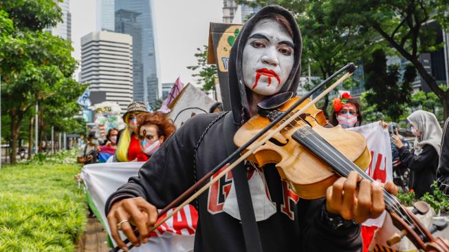 Seorang massa demonstrasi bermain musik saat mengikuti aksi darurat iklim di Jalan Sudirman, Jakarta Pusat, Jumat (25/3/2022). [Suara.com/Alfian Winanto]