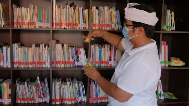 Umat Hindu memercikkan air suci saat melakukan penyucian terhadap ribuan buku ilmu pengetahuan dalam rangkaian persembahyangan Hari Saraswati di Perpustakaan Sabha Widya Sradha, Desa Sumerta Kelod, Denpasar, Bali, Sabtu (26/3/2022). [ANTARA FOTO/Nyoman Hendra Wibowo/nym]
