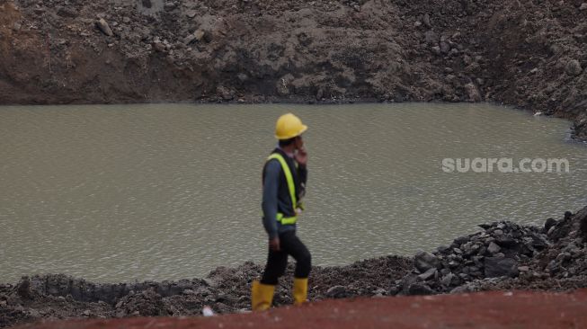 Pekerja berjalan di dekat lahan yang akan dijadikan Waduk Brigif, Jagakarsa, Jakarta, Minggu (27/3/2022). [Suara.com/Angga Budhiyanto]