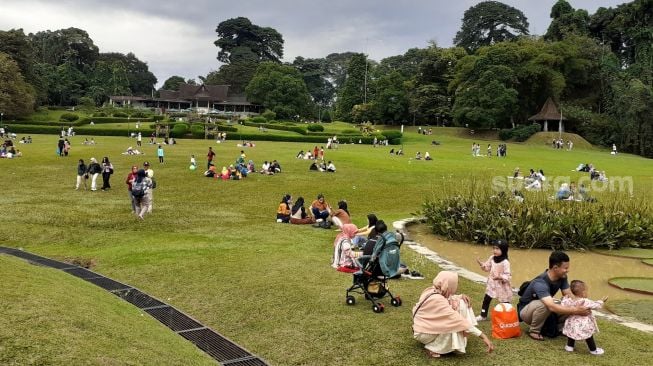 Suasana pengunjung piknik di halaman Kebun Raya Bogor, Bogor ,jawa Barat, Minggu (27/3/2022).  [Suara.com/Septian]