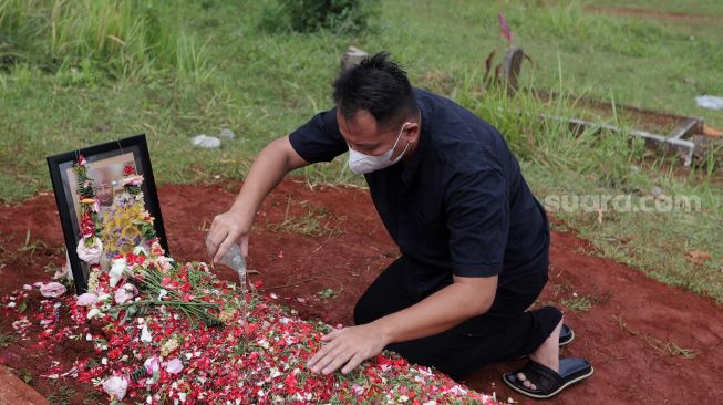 Presenter Vicky Prasetyo menyiramkan air kembang ke makam ibunda Kalina Oktarani, Erlan Wardhania di TPU Taman Abadi, Ciputat, Tangerang Selatan, Banten, Senin (28/3/2022). [Suara.com/Angga Budhiyanto]