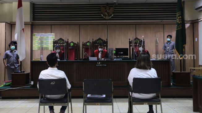 Terdakwa Adam Deni (kiri) dan Ni Made Dwita Anggari mengikuti sidang dengan agenda pembacaan putusan sela kasus pelanggaran Undang-Undang ITE di Pengadilan Negeri Jakarta Utara, Jakarta, Selasa (29/3/2022). [Suara.com/Angga Budhiyanto]