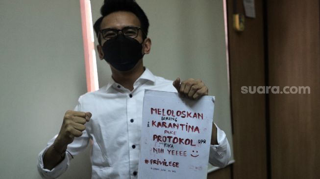 Terdakwa Adam Deni menunjukkan poster tanda protes sebelum mengikuti sidang dengan agenda pembacaan putusan sela kasus pelanggaran Undang-Undang ITE di Pengadilan Negeri Jakarta Utara, Jakarta, Selasa (29/3/2022). [Suara.com/Angga Budhiyanto]