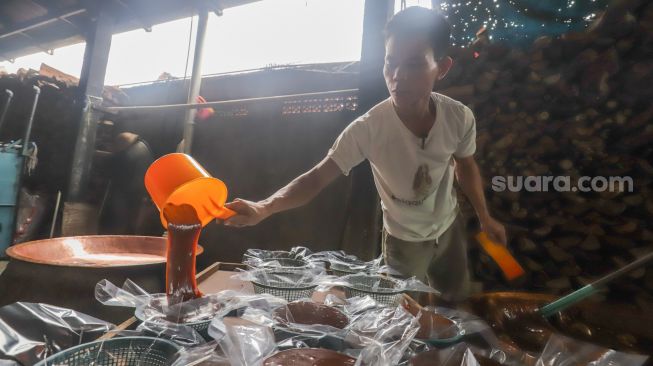 Pekerja menuang dodol betawi ke dalam wadah di rumah produksi Dodol Betawi Sari Rasa Ibu Yuyun, Jakarta Selatan, Kamis (31/3/2022). [Suara.com/Alfian Winanto]