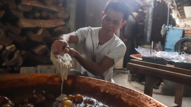 Pekerja menuang adonan dodol betawi ke dalam kuali di rumah produksi Dodol Betawi Sari Rasa Ibu Yuyun, Jakarta Selatan, Kamis (31/3/2022). [Suara.com/Alfian Winanto]