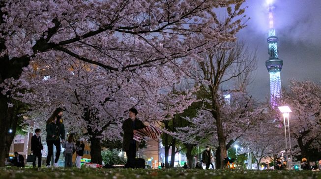 Orang-orang berkumpul untuk melihat bunga sakura dengan latar belakang Tokyo Skytree (kanan) di Taman Kinshi distrik Sumida di Tokyo, Jepang, Selasa (29/3/2022). [Philip FONG / AFP]
