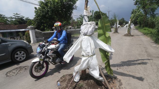 Pengendara sepeda motor melintas di jalan rusak yang ditanami tanaman pisang dan tebu di Desa Janti, Kediri, Jawa Timur, Sabtu (2/4/2022). [ANTARA FOTO/Prasetia Fauzani/foc]