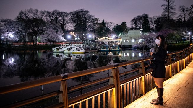 Seorang wanita melihat bunga sakura yang bermekaran di Taman Inokashira, Tokyo, Jepang, Rabu (30/3/2022). [Philip FONG / AFP]