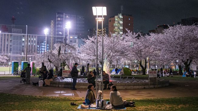 Orang-orang berkumpul untuk melihat bunga sakura dengan latar belakang Tokyo Skytree (kanan) di Taman Kinshi distrik Sumida di Tokyo, Jepang, Selasa (29/3/2022). [Philip FONG / AFP]
