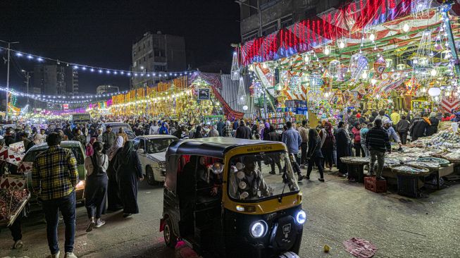 Sebuah kendaraan tuk-tuk melewati pasar yang menjual lentera dan dekorasi Ramadhan lainnya di distrik Sayyida Zeinab, Kairo, Mesir, Rabu (30/3/2022). [Khaled DESOUKI / AFP]