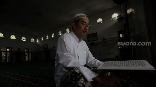 Pengurus Masjid Jami Maulana Hasanuddin, Fachrie Aie (30) membaca ayat suci Al-Qur'an di dalam area masjid, Cikoko, Pancoran, Jakarta, Minggu (3/4/2022). [Suara.com/Angga Budhiyanto]