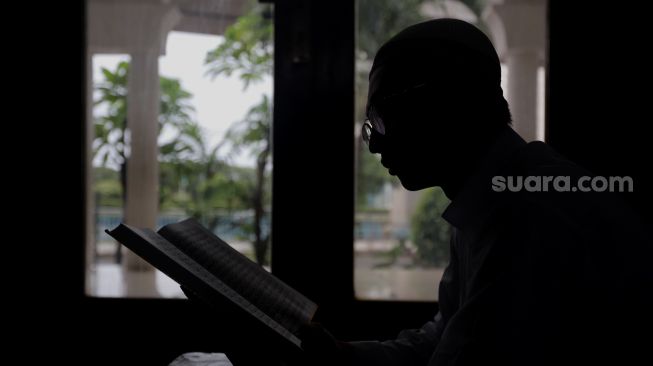 Siluet pengurus Masjid Jami Maulana Hasanuddin, Fachrie Aie (30) membaca ayat suci Al-Qur'an di dalam area masjid, Cikoko, Pancoran, Jakarta, Minggu (3/4/2022). [Suara.com/Angga Budhiyanto]