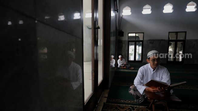 Pengurus Masjid Jami Maulana Hasanuddin, Fachrie Aie (30) membaca ayat suci Al-Qur'an di dalam area masjid, Cikoko, Pancoran, Jakarta, Minggu (3/4/2022). [Suara.com/Angga Budhiyanto]