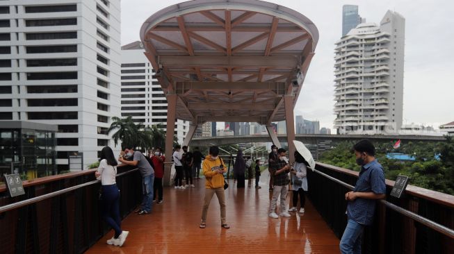 Warga menikmati suasana di Jembatan Penyeberangan Orang (JPO) Pinisi Karet-Sudirman, Jakarta, Minggu (3/4/2022). [Suara.com/Angga Budhiyanto]