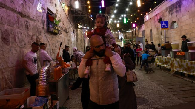 Warga Palestina berjalan menyusuri jalan di Kota Tua Yerusalem, Sabtu (2/4/2022). [Menahem KAHANA / AFP]
