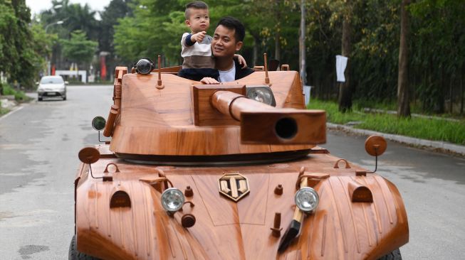 Truong Van Dao dan putranya mengendarai tank kayu yang terbuat minibus tua di sebuah daerah perumahan di provinsi Bac Ninh, Vietnam, Senin (28/3/2022). [Nhac NGUYEN / AFP]
