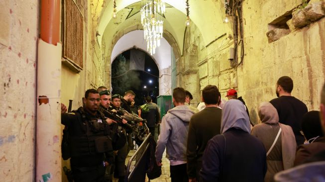 Pasukan keamanan Israel berjaga-jaga ketika warga Palestina berjalan di jalan di Kota Tua Yerusalem, Sabtu (2/4/2022). [Menahem KAHANA / AFP]