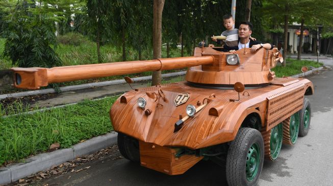 Truong Van Dao dan putranya mengendarai tank kayu yang terbuat minibus tua di sebuah daerah perumahan di provinsi Bac Ninh, Vietnam, Senin (28/3/2022). [Nhac NGUYEN / AFP]