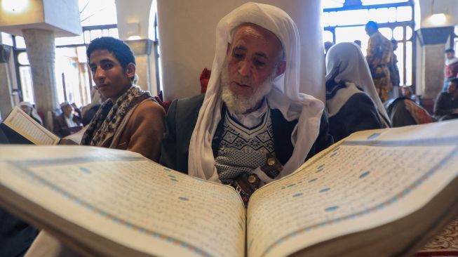 Seorang pria Muslim mendengarkan ketika seorang anak membaca Alquran di Masjid Al-Kabir, Sana'a, Yaman, Sabtu (2/4/2022). [MOHAMMED HUWAIS / AFP]