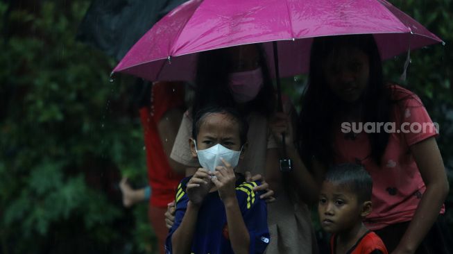 Warga menggunakan payung untuk berlindung dari hujan saat mengantre untuk mendapatkan takjil gratis di Jalan Cempaka Putih Tengah XXI, Jakarta, Selasa (5/4/2022). [Suara.com/Angga Budhiyanto]