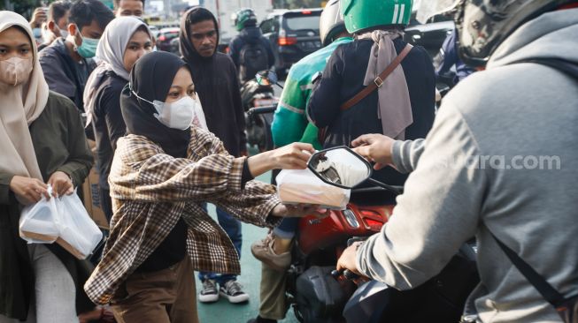 Massa membagikan Takjil pada pengendara saat menggelar aksi demonstrasi menuntut proses hukum Tan Paulin di depan Gedung DPR RI, Jakarta Pusat, Rabu (6/4/2022). [Suara.com/Alfian Winanto]