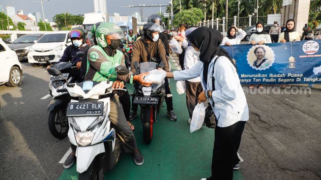 Massa membagikan Takjil pada pengendara saat menggelar aksi demonstrasi menuntut proses hukum Tan Paulin di depan Gedung DPR RI, Jakarta Pusat, Rabu (6/4/2022). [Suara.com/Alfian Winanto]