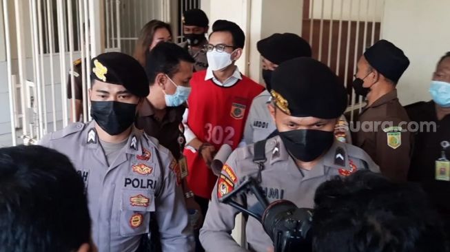 Adam Deni dikawal polisi jelang sidang di Pengadilan Negeri Jakarta Pusat, Rabu (6/4/2022). [Evi Ariska/Suara.com]