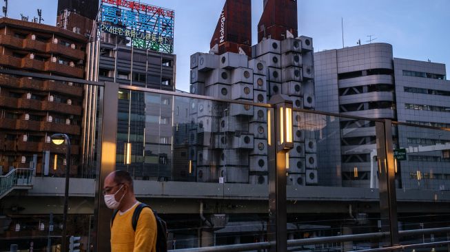 Seorang pria berjalan di sepanjang Jembatan Penyeberangan Orang (JPO) dengan latar belakang Menara Kapsul Nakagin (tengah) di distrik Ginza, Tokyo, Jepang, Rabu (6/4/2022). [Philip FONG / AFP]
