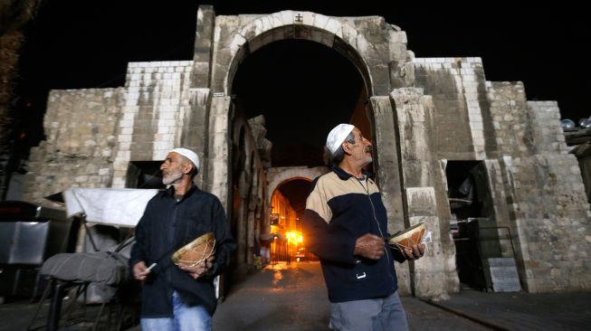 Dua orang Mesaharati menabuh gendang dan menyanyikan lagu-lagu religi sambil berkeliling membangunkan warga untuk sahur di Damaskus, Suriah, Kamis (7/4/2022). [LOUAI BESHARA / AFP]
