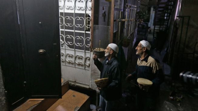 Dua orang Mesaharati menabuh gendang dan menyanyikan lagu-lagu religi sambil berkeliling membangunkan warga untuk sahur di Damaskus, Suriah, Kamis (7/4/2022). [LOUAI BESHARA / AFP]
