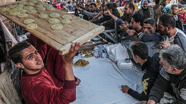 Pedagang membawa nampan berisi Qatayef (pangsit tradisional Arab) untuk pelanggan saat bulan Ramadhan di Gaza, Palestina, Minggu (3/4/2022). [Said Khatib / AFP]