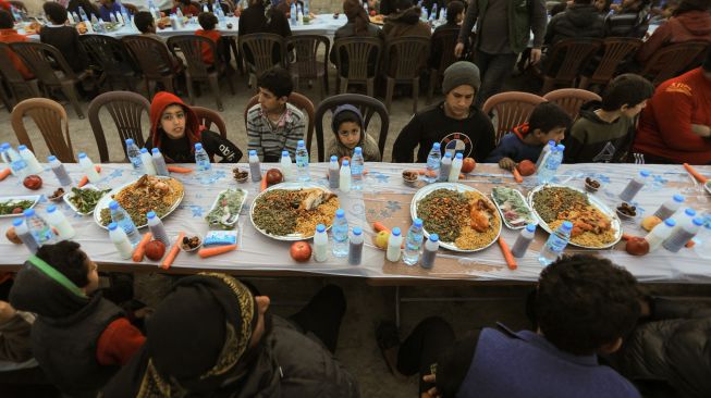 Anak-anak pengungsi Suriah berbagi makanan berbuka puasa bersama saat bulan suci Ramadhan di Kota Al-Bab, provinsi Aleppo, Suriah, Kamis (7/4/2022). [Bakr ALKASEM / AFP]
