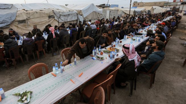 Pengungsi Suriah berbagi makanan berbuka puasa bersama saat bulan suci Ramadhan di Kota Al-Bab, provinsi Aleppo, Suriah, Kamis (7/4/2022). [Bakr ALKASEM / AFP]