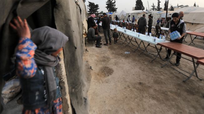 Seorang anak melihat saat para sukarelawan menyiapkan meja bagi pengungsi Suriah untuk berbagi makanan berbuka puasa bersama saat bulan suci Ramadhan di Kota Al-Bab, provinsi Aleppo, Suriah, Kamis (7/4/2022). [Bakr ALKASEM / AFP]