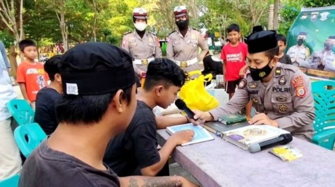 Petugas menghukum pelaku balap liar berusia remaja dengan mengaji Al Quran saat terjaring operasi Kamtibmas di Jalan Cekkeng Nursery, Kabupaten Bone, Sulawesi Selatan, Sabtu (9/4/2022). [Dok. Polisi]