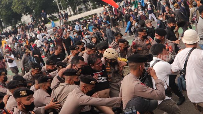 Polisi mengamankan salah seorang massa yang dikeroyok saat ricuh di depan depan gedung DPR RI, Jakarta, Senin (11/4/2022). [Suara.com/Angga Budhiyanto]