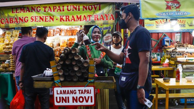 Warga membeli Lemang untuk berbuka puasa di Sentra kuliner Nasi Kapau di Jalan Kramat Raya, Senen, Jakarta Pusat, Selasa (12/4/2021). [Suara.com/Alfian Winanto]